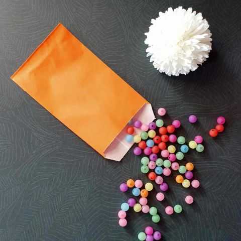 Petit sachet kraft orange garni de perles de couleur. Emballage idéal pour les petits objets.