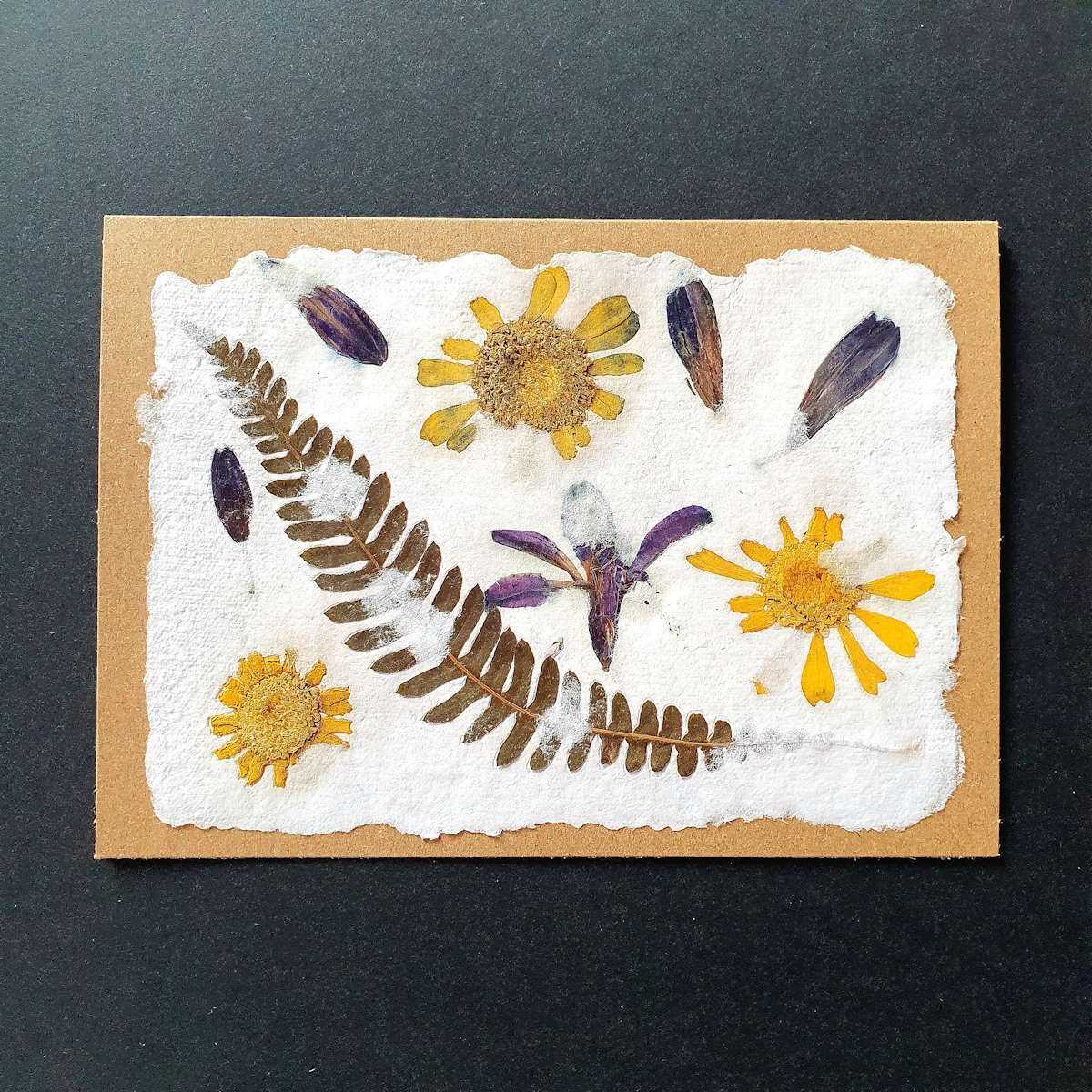 Carte double en papier artisanal avec inclusions florales.